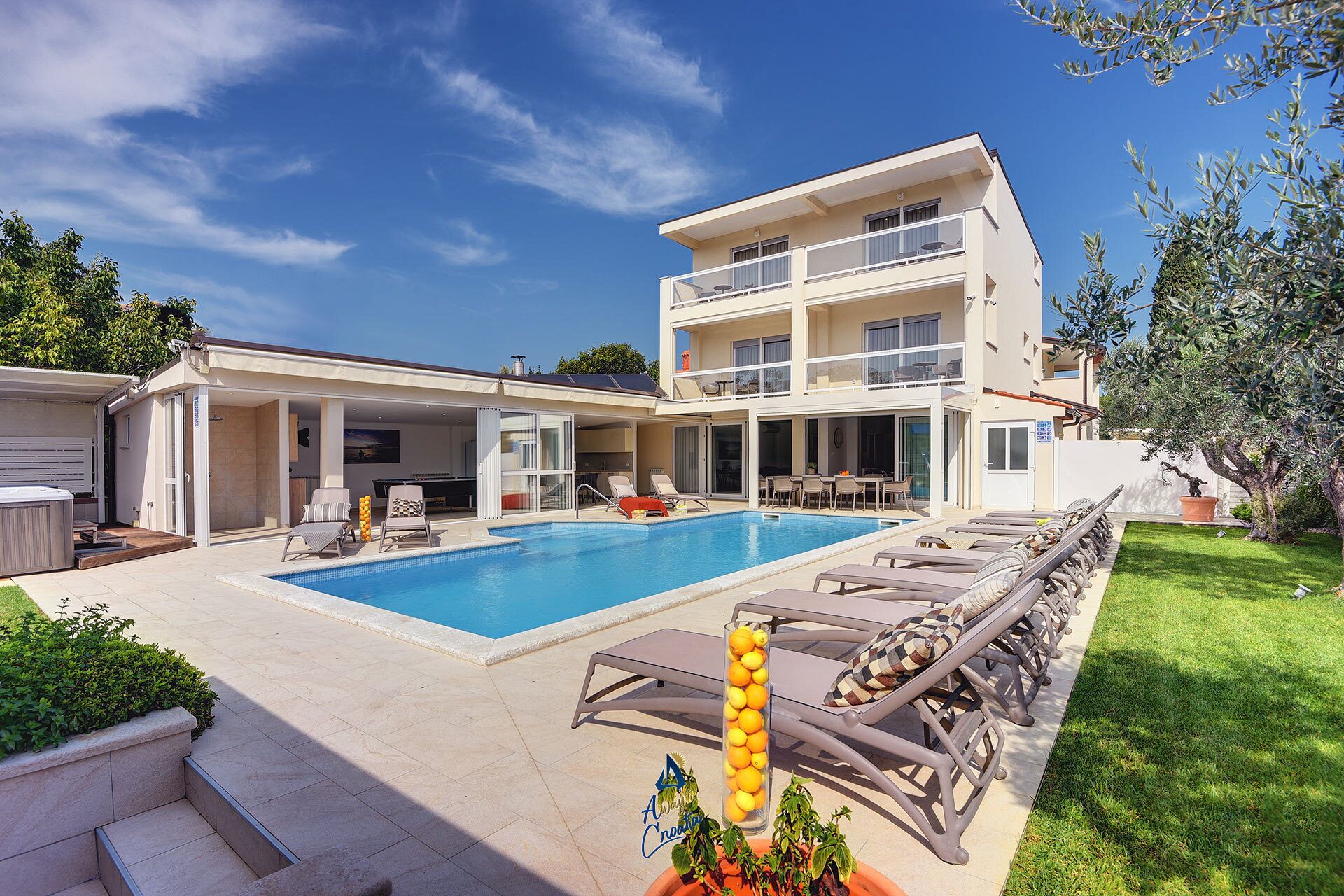 A two-story building with a swimming pool, outdoor seating, and a well-maintained lawn.