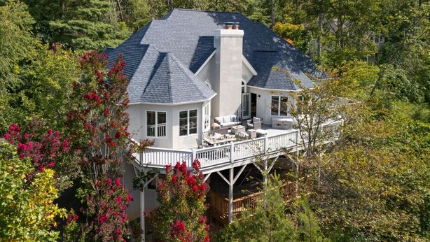 Une grande maison dotée d’une terrasse couverte, entourée d’arbres et d’arbustes.