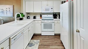 A modern kitchen with white cabinetry, a microwave, an oven, and a refrigerator. - Dolphin Watch 7 Tybee Vacation Rentals (Tybee Island)