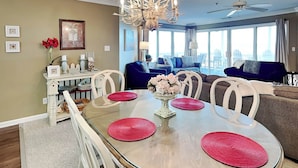 A dining area with a glass table, red placemats, and a chandelier. - Dolphin Watch 7 Tybee Vacation Rentals (Tybee Island)