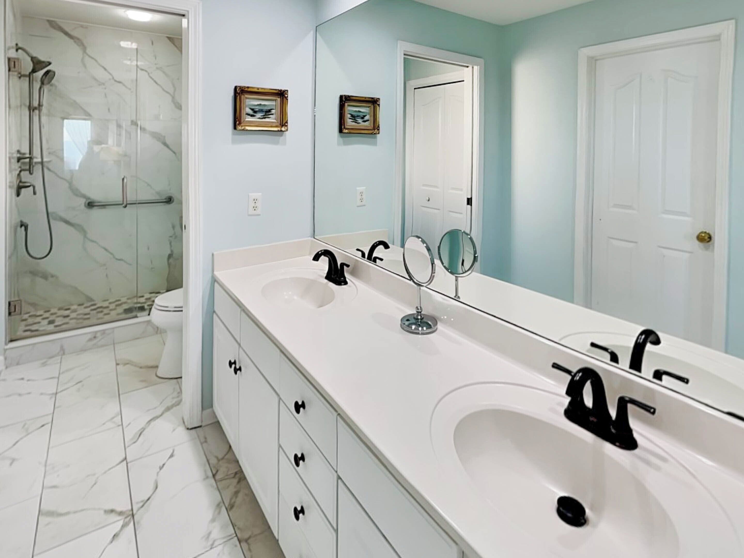 A bathroom with a large mirror, two sinks, and a shower area.