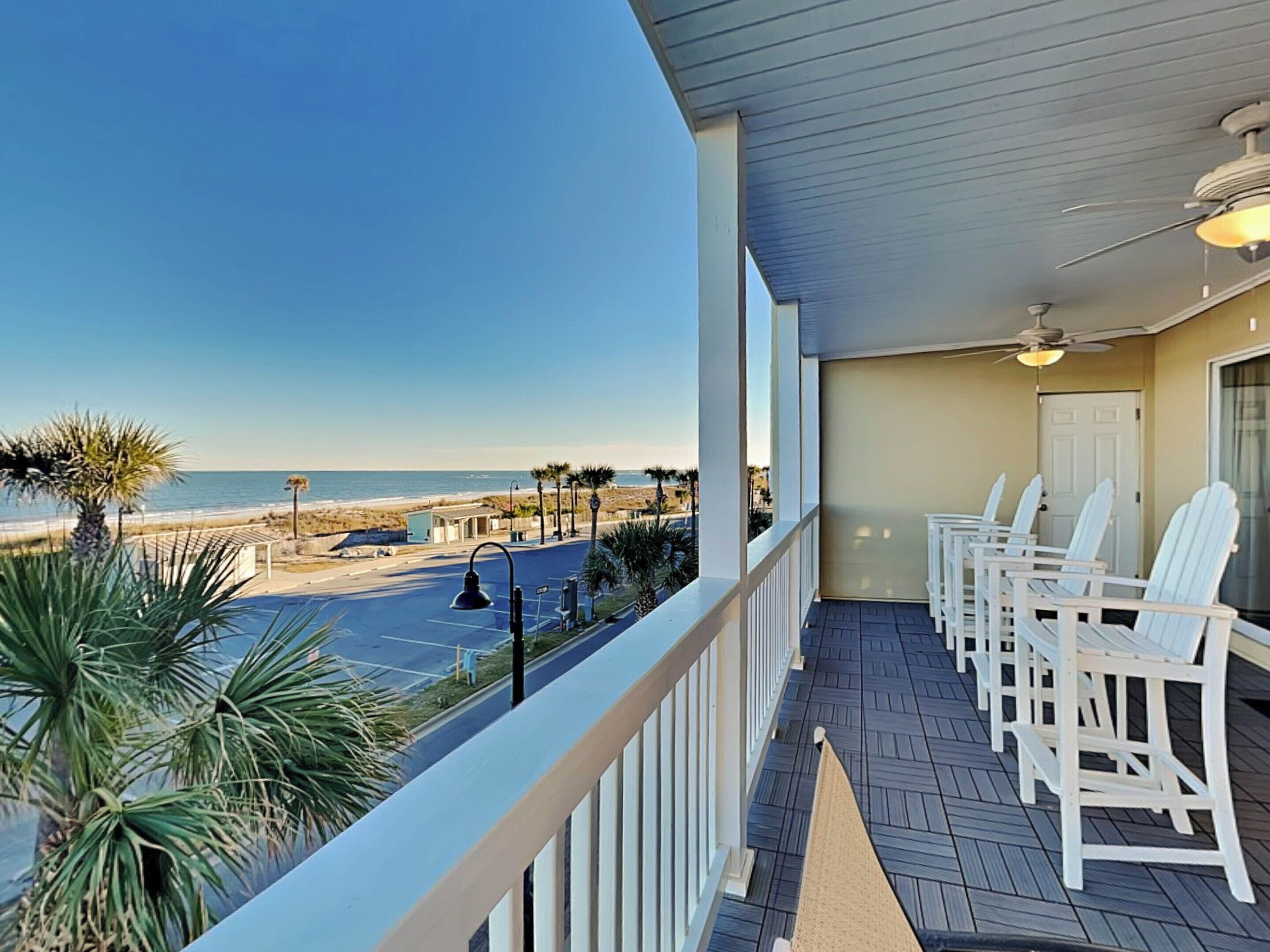 A balcony with white chairs, a ceiling fan, and a view of the beach.