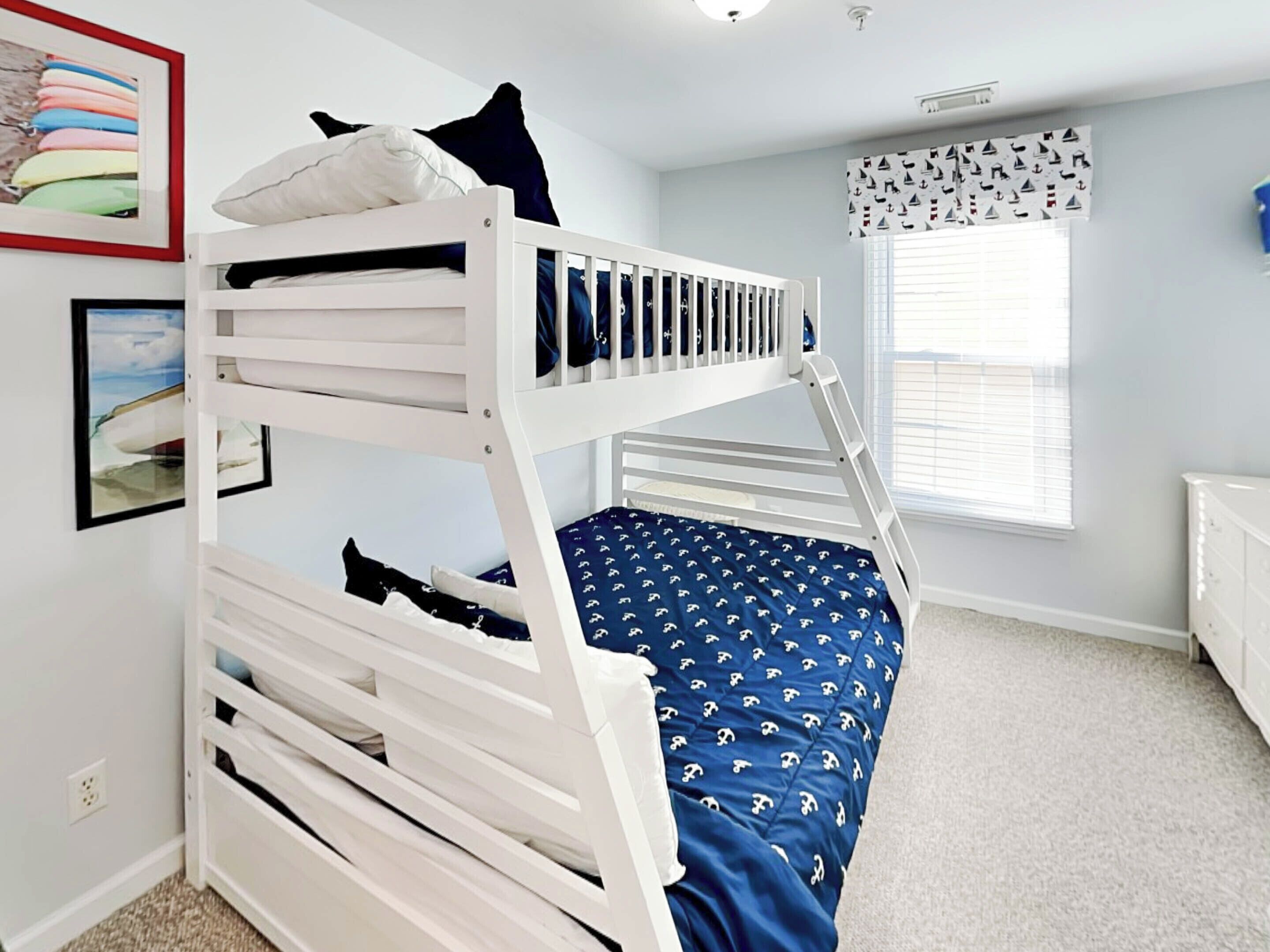 A bunk bed room with a window, a framed picture, and a white dresser.