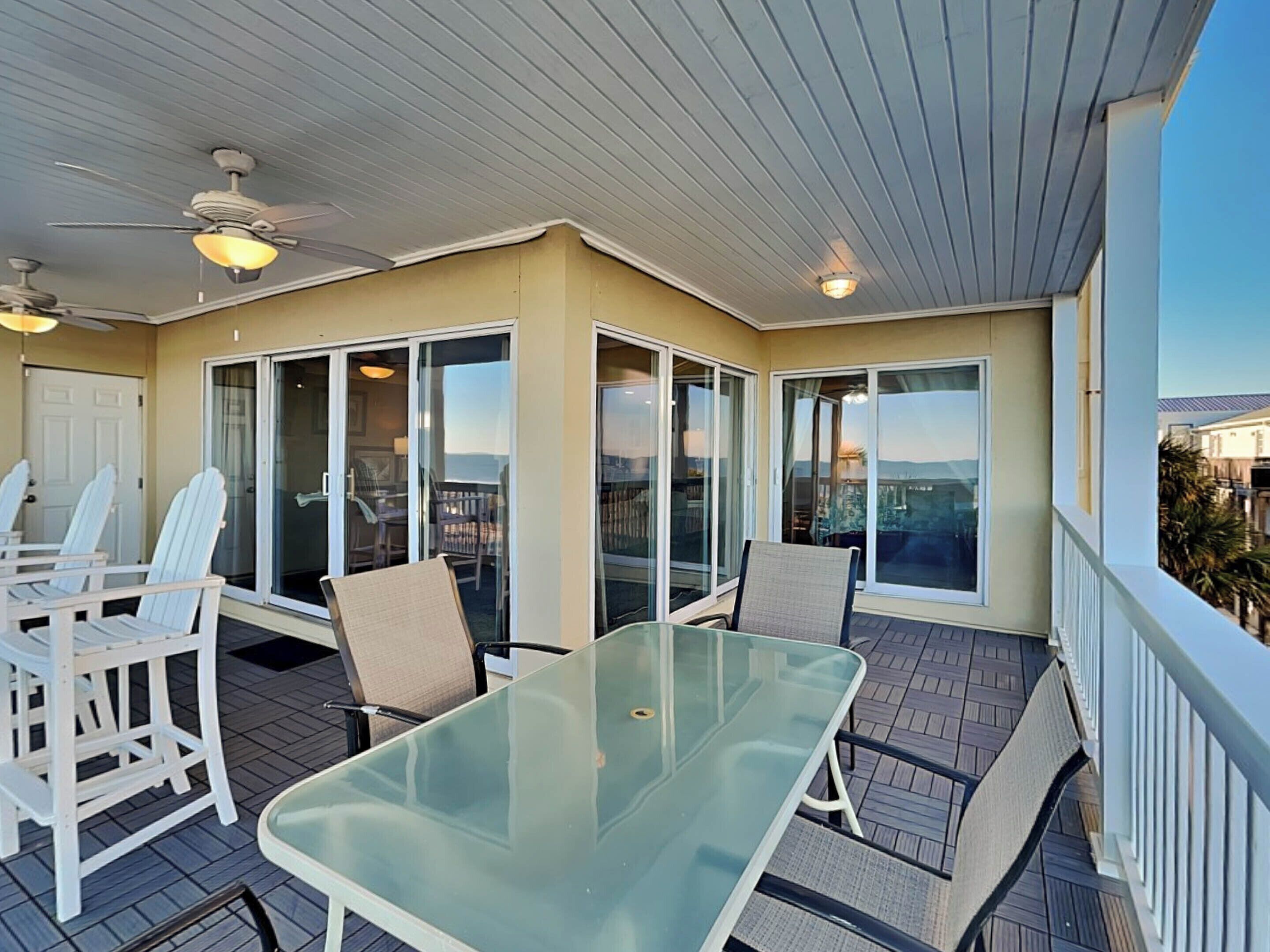 A covered outdoor area with a glass table and chairs, sliding glass doors, and ceiling fans.