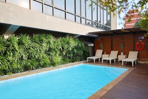 Una piscina con lettini, un muro di legno con piante e un edificio moderno sullo sfondo.