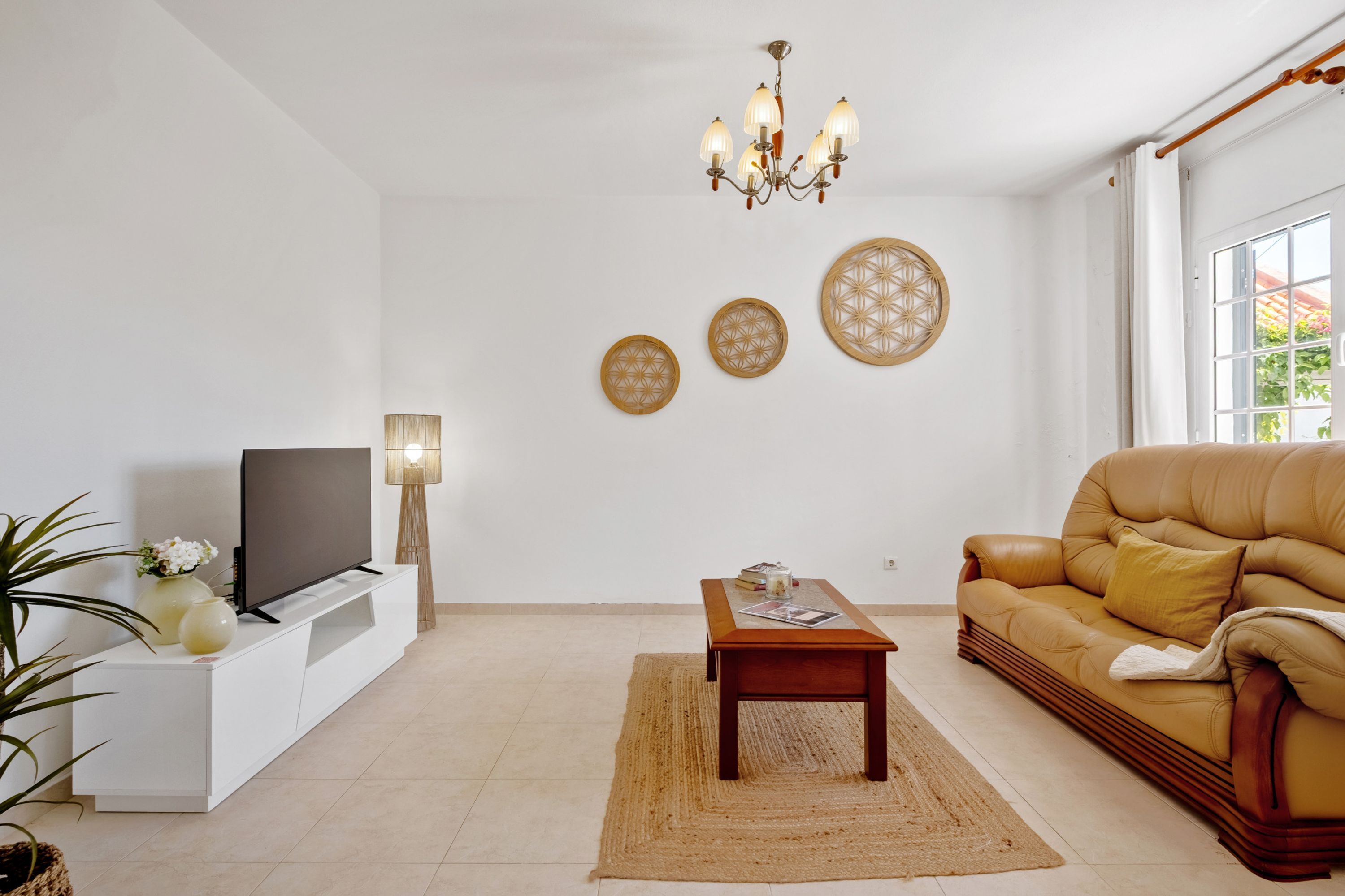A living room with a flat-screen TV, a wooden coffee table, a sofa, a chandelier, and decorative wall art.