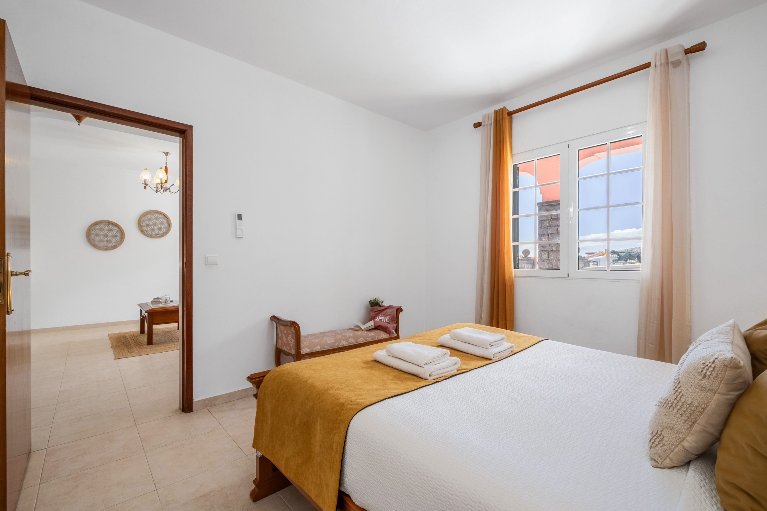 Un dormitorio con cama, una ventana con cortinas, un escritorio con silla y una puerta que da a otra habitación.