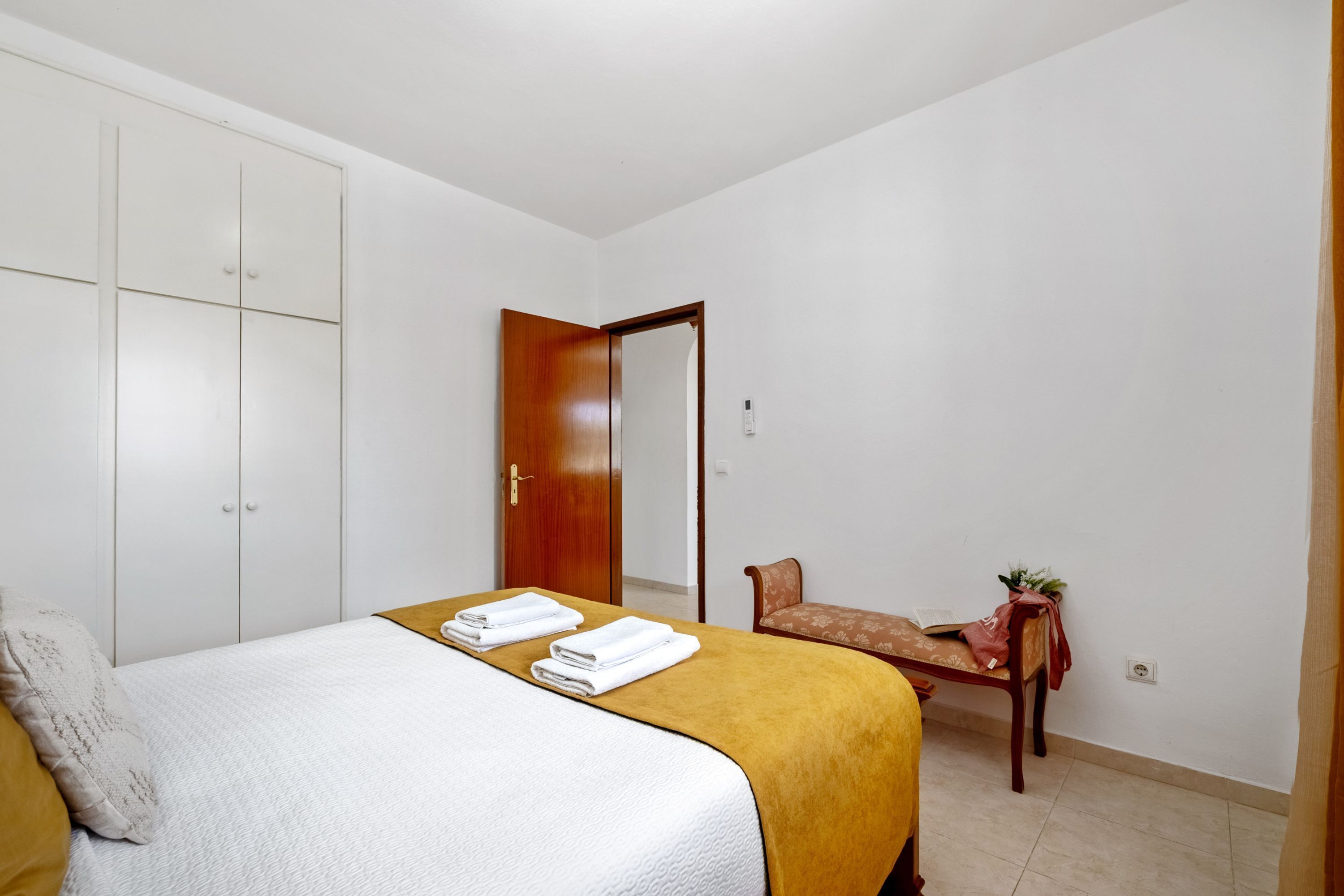 A bedroom with a bed, a wooden wardrobe, a bench, and a small table with a plant.