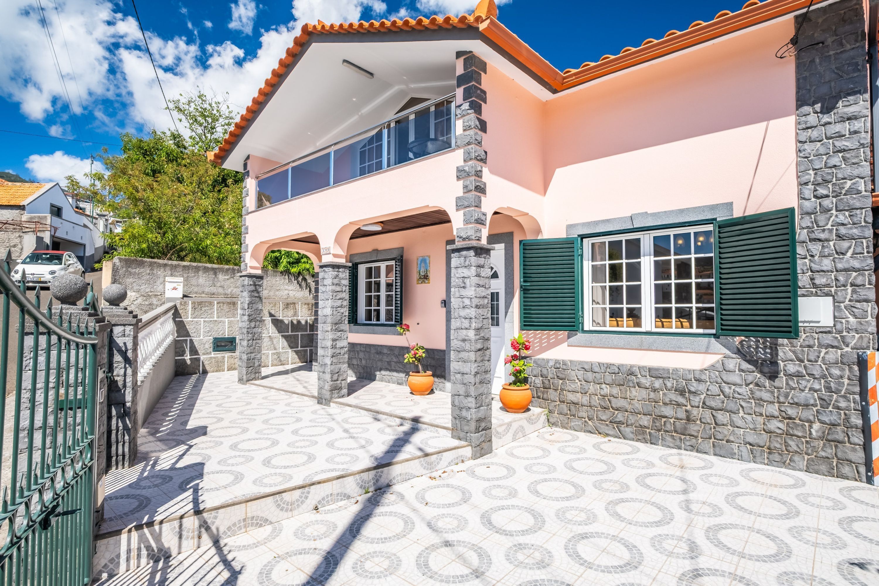 A two-story house with a stone facade, a tiled patio, and a car parked in front.