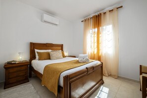 A neatly arranged bedroom with a wooden bed, a bedside table with a lamp, and a window with curtains. - Golden Coast A by Homie (Calheta)
