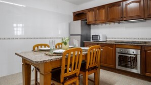 A modern kitchen with wooden cabinets, granite countertops, stainless steel appliances, and a dining area with wooden chairs and a granite table. - Golden Coast A by Homie (Calheta)