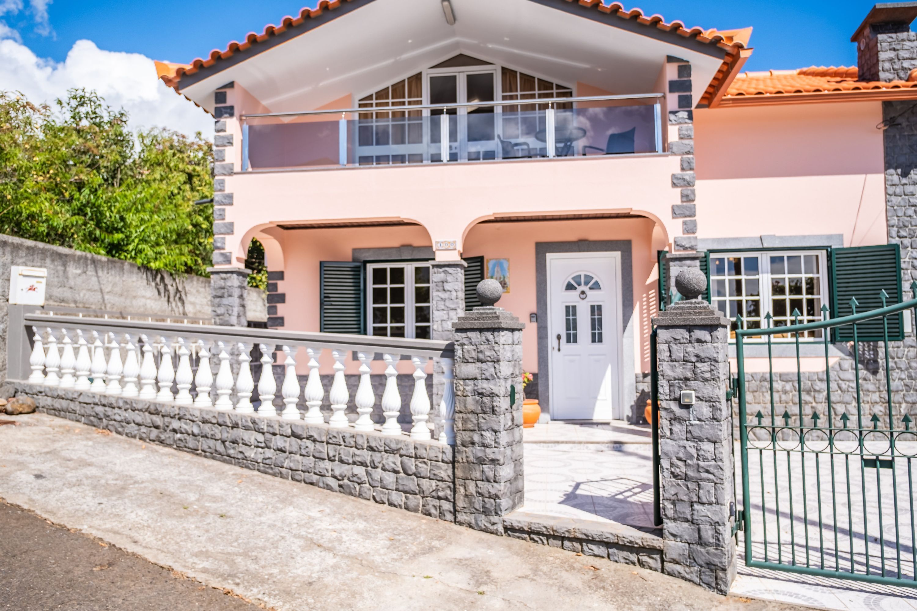 A two-story house with a balcony, a stone facade, and a gated entrance.