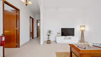 Una sala de estar moderna con televisor, una mesa de centro, una planta en maceta y una lámpara.