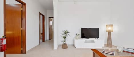 A modern living room with a television, a coffee table, a potted plant, and a lamp.