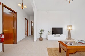 A modern living room with a television, a coffee table, a potted plant, and a lamp. - Golden Coast A by Homie (Calheta)