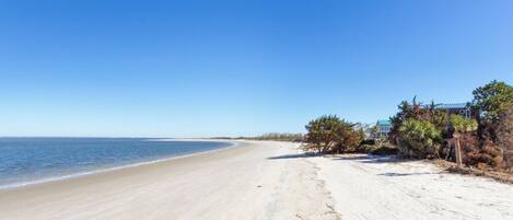 A beach with a clear sky, sandy shore, and a building with a green roof.