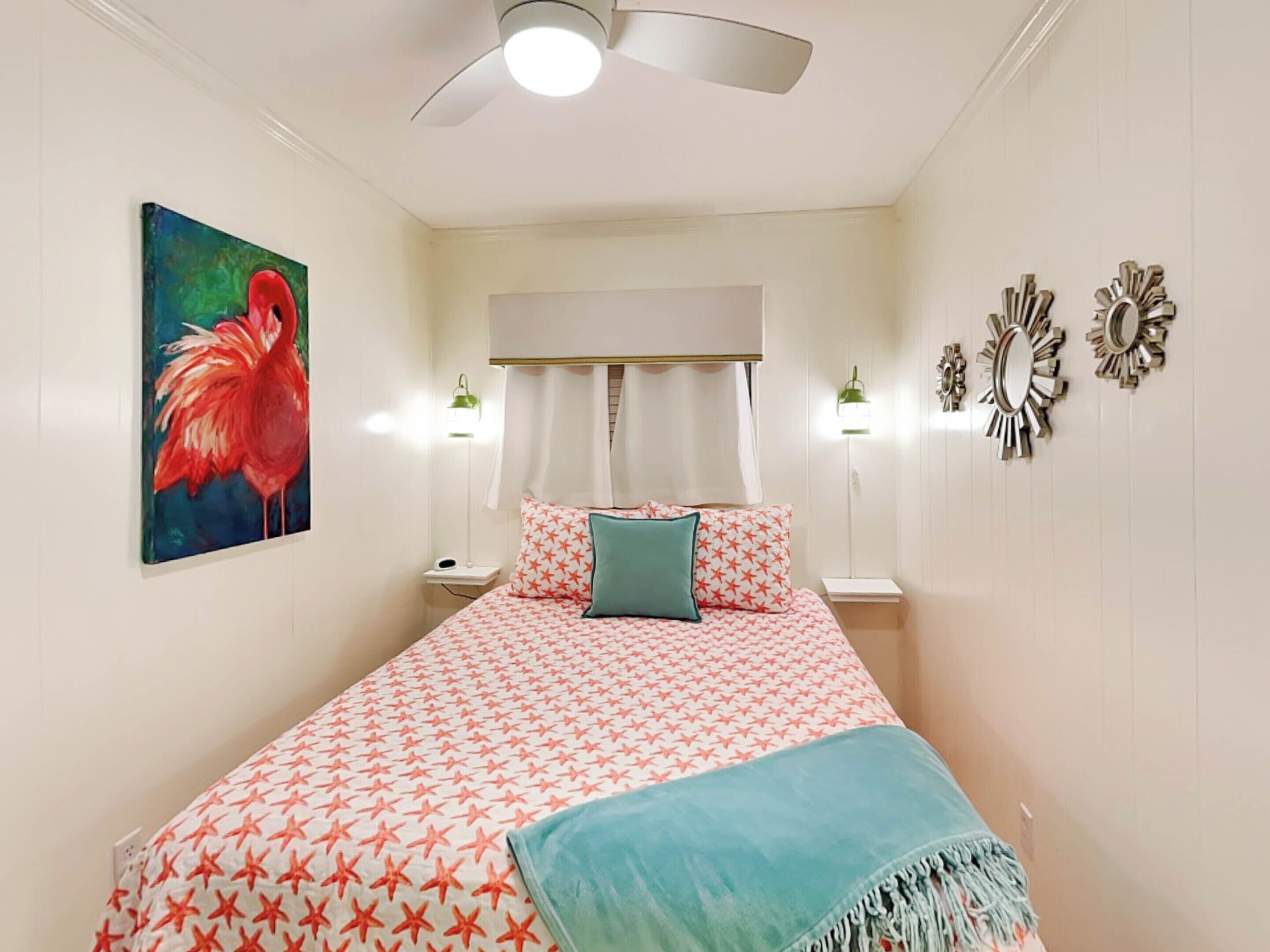 A bedroom with a bed, a ceiling fan, a painting, two bedside lamps, and wall decorations.