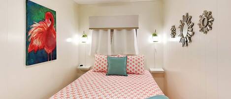 A bedroom with a bed, a ceiling fan, a painting, two bedside lamps, and wall decorations.