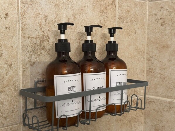 Un estante en el baño con tres botellas de crema corporal, champú y acondicionador.
