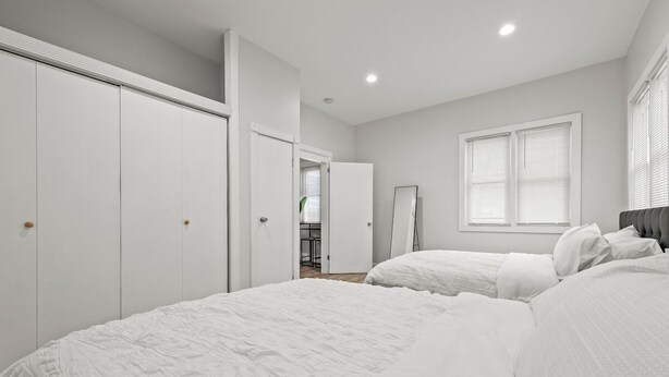 A bedroom with two beds, white wardrobes, a mirror, and a window with blinds.