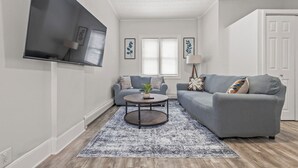 A living room with a grey sofa, a round coffee table, and a TV mounted on the wall.