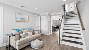 A modern living room with a beige sofa, a coffee table, and a wooden staircase.