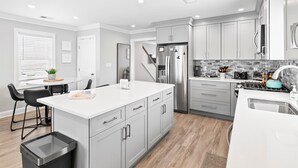 A modern kitchen with white cabinets, a stainless steel refrigerator, and a black trash bin.
