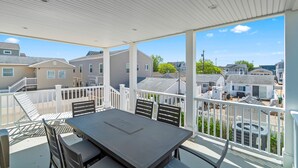 A covered outdoor patio with a table and chairs, white railings, and a view of neighboring houses.