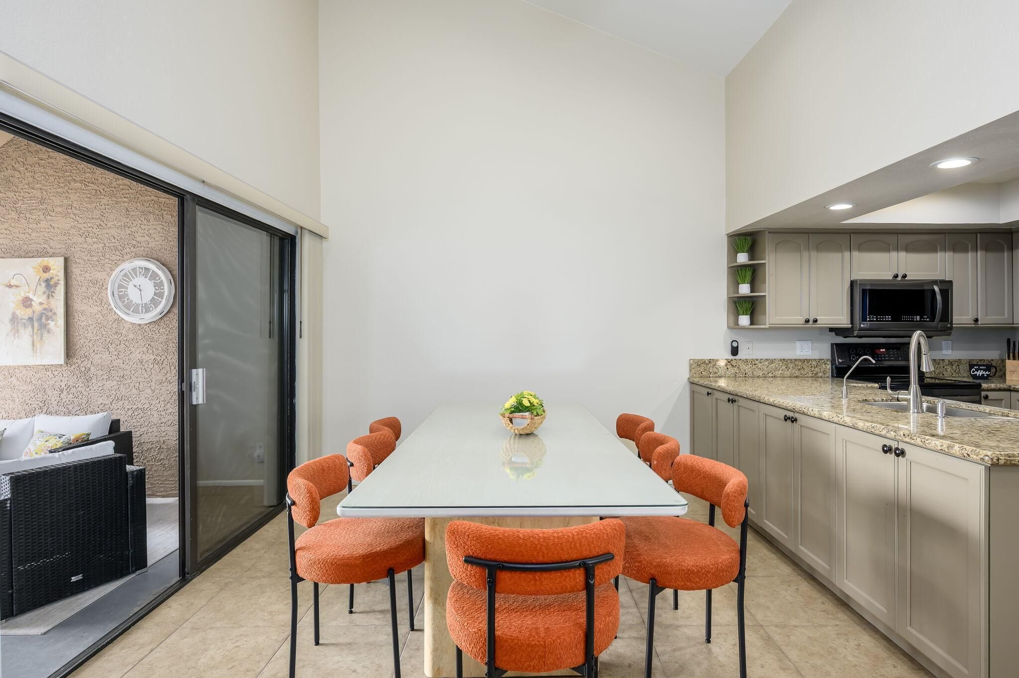 Une cuisine moderne dotée d’un grand îlot central, d’appareils électroménagers intégrés et d’un coin repas avec une table en verre et des chaises orange.