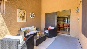 Un espace extérieur aménagé en terrasse, avec des meubles en osier, une table basse en verre et un tableau représentant des tournesols.