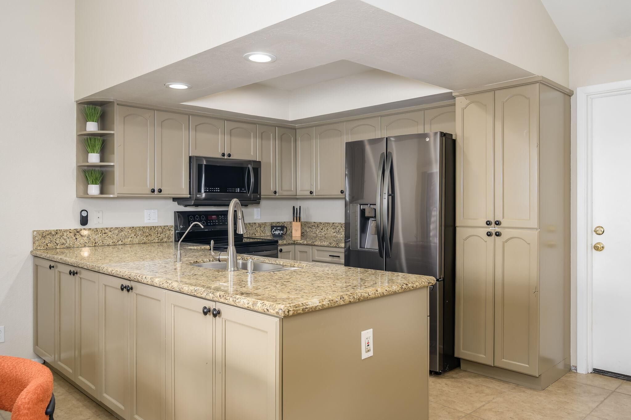 Una cocina con gabinetes color beige, encimeras de granito y electrodomésticos de acero inoxidable, incluyendo un microondas integrado.