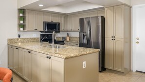 Une cuisine avec des meubles de couleur beige, des comptoirs en granit, des appareils électroménagers en acier inoxydable et un four à micro-ondes encastré.