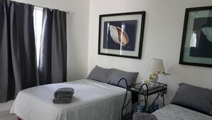 Ein Hotelzimmer mit zwei Betten, gestreifter Bettwäsche, einem gerahmten Bild an der Wand, einem Nachttisch mit Lampe und einem Fenster mit Vorhängen.