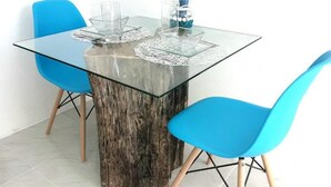 Ein Esstisch mit Glasplatte und Holzfuß, umgeben von zwei blauen Stühlen mit Holzbeinen.