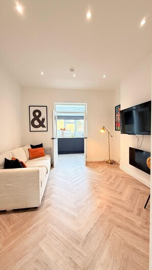 Uma sala de estar moderna com um sofá, uma televisão e um chão com padrão herringbone.