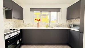 A modern kitchen with dark cabinets, a marble backsplash, a built-in oven, a sink, and a window with a view of yellow buildings. - Stylish apartment close to center zone 2, London, UK (London)