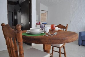 A round wooden dining table with white plates, a green placemat, and a white pitcher. - Hacienda Vallarta - Los Muertos Beach (Puerto Vallarta)