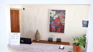 A reception area with a wooden door, a welcome sign, a vase, a colorful painting, a small table with remotes, and a potted plant. - Hacienda Vallarta - Los Muertos Beach (Puerto Vallarta)