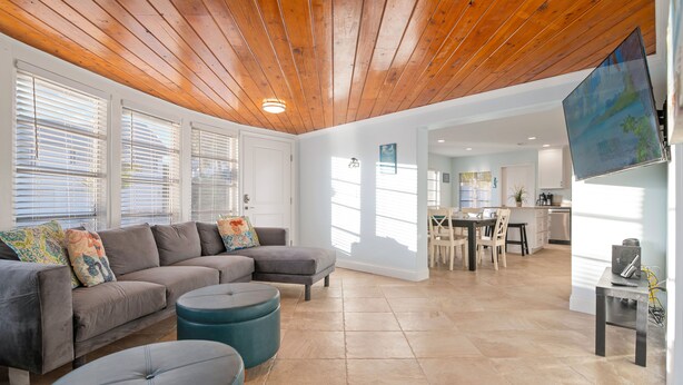 A spacious living area with a wooden ceiling, a gray sectional sofa, teal ottomans, and a kitchen in the background. - ⚓Mermaid Sunset! Coastal beach home w/pool 200 steps to beach!⚓ (Holmes Beach)