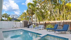 A swimming pool with lounge chairs and a barbecue area, surrounded by palm trees and a wooden fence. - ⚓Mermaid Sunset! Coastal beach home w/pool 200 steps to beach!⚓ (Holmes Beach)