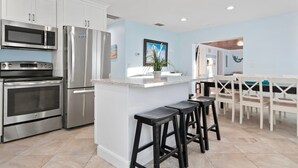 A modern kitchen with stainless steel appliances, a light blue wall, and a central island with bar stools. - ⚓Mermaid Sunset! Coastal beach home w/pool 200 steps to beach!⚓ (Holmes Beach)