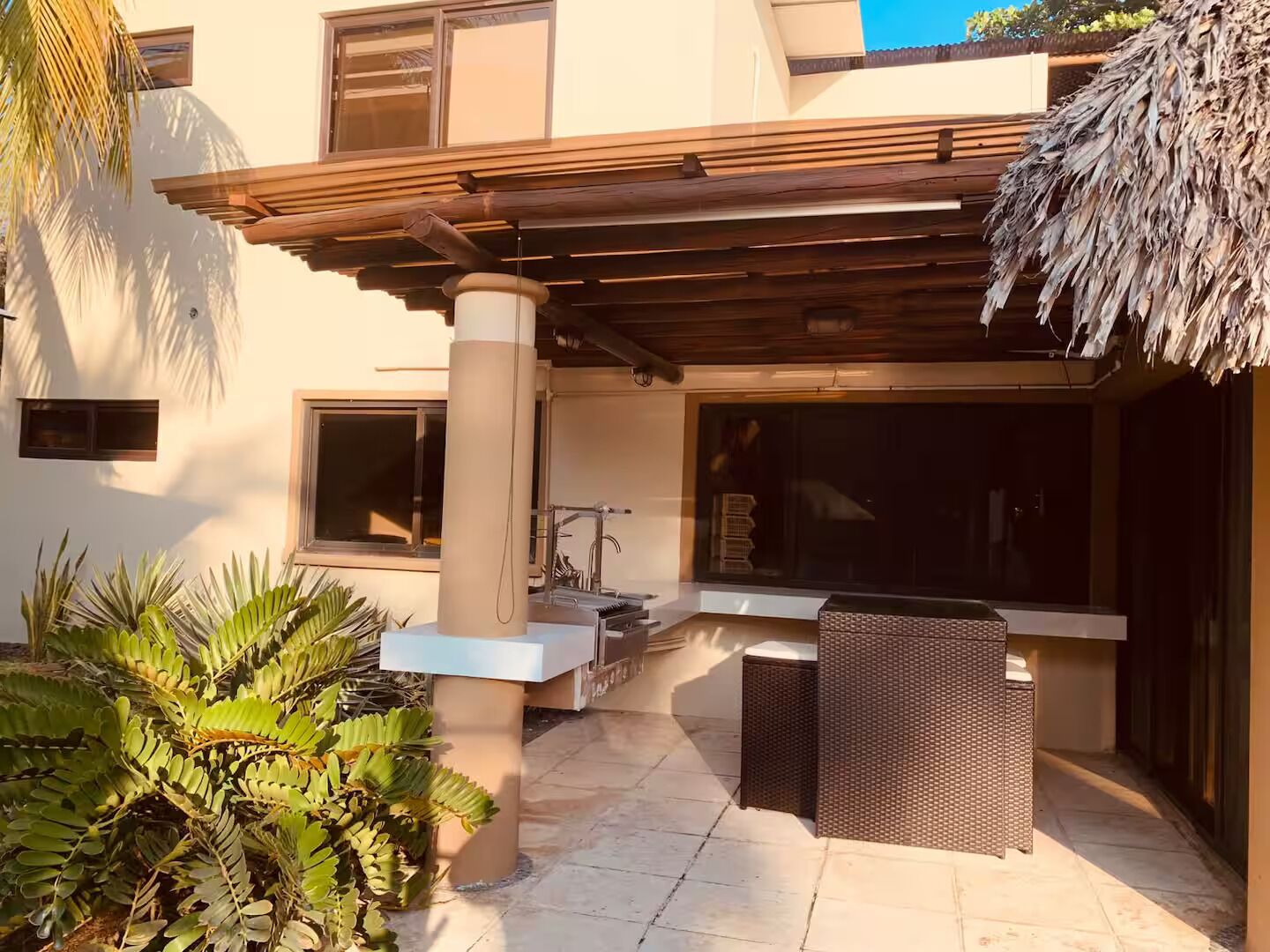 Un patio techado al aire libre con una pérgola, una zona de estar con mesa y sillas, y un ventanal grande.