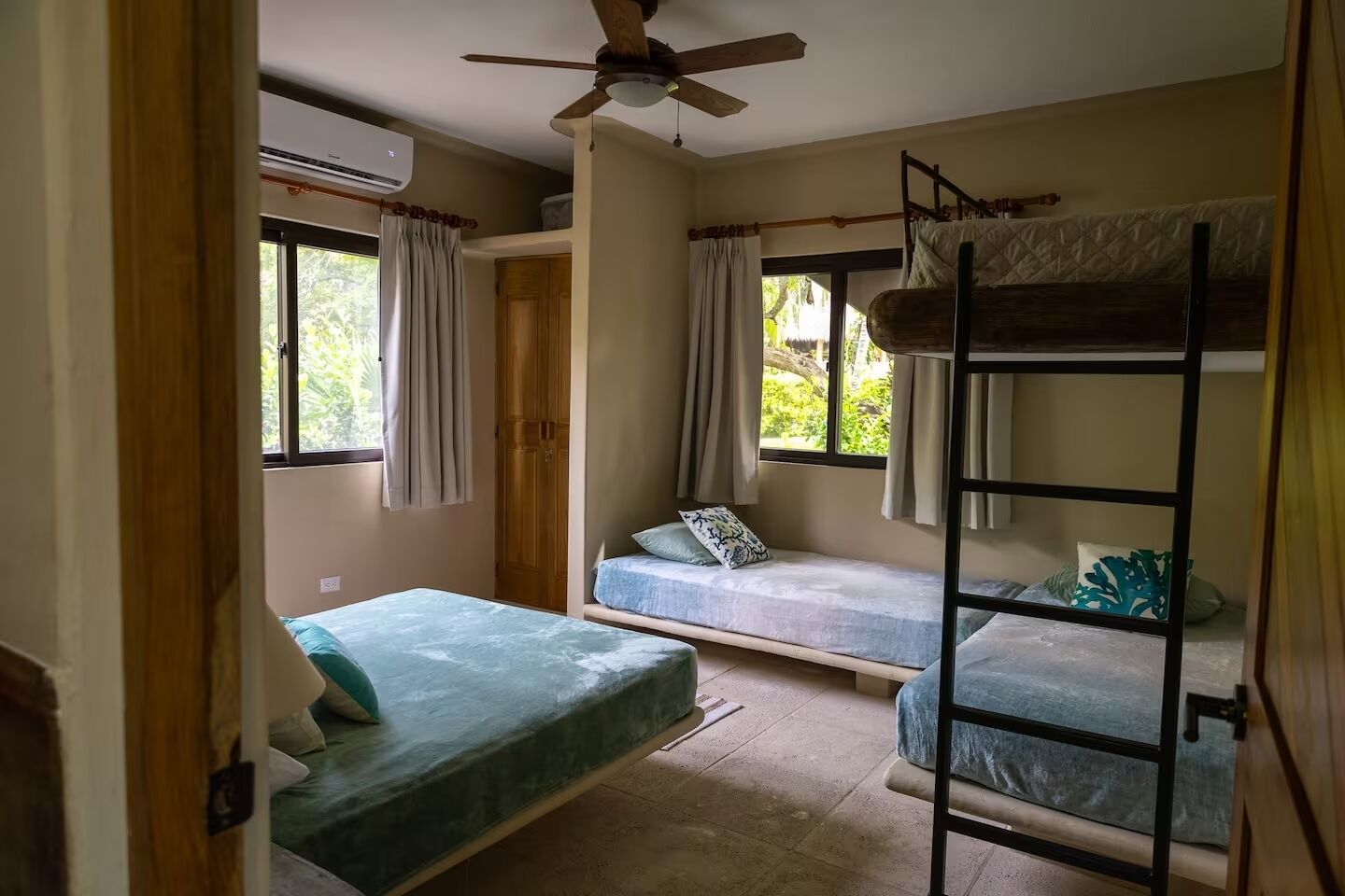 A dormitory room with bunk beds, a ceiling fan, and windows with curtains.