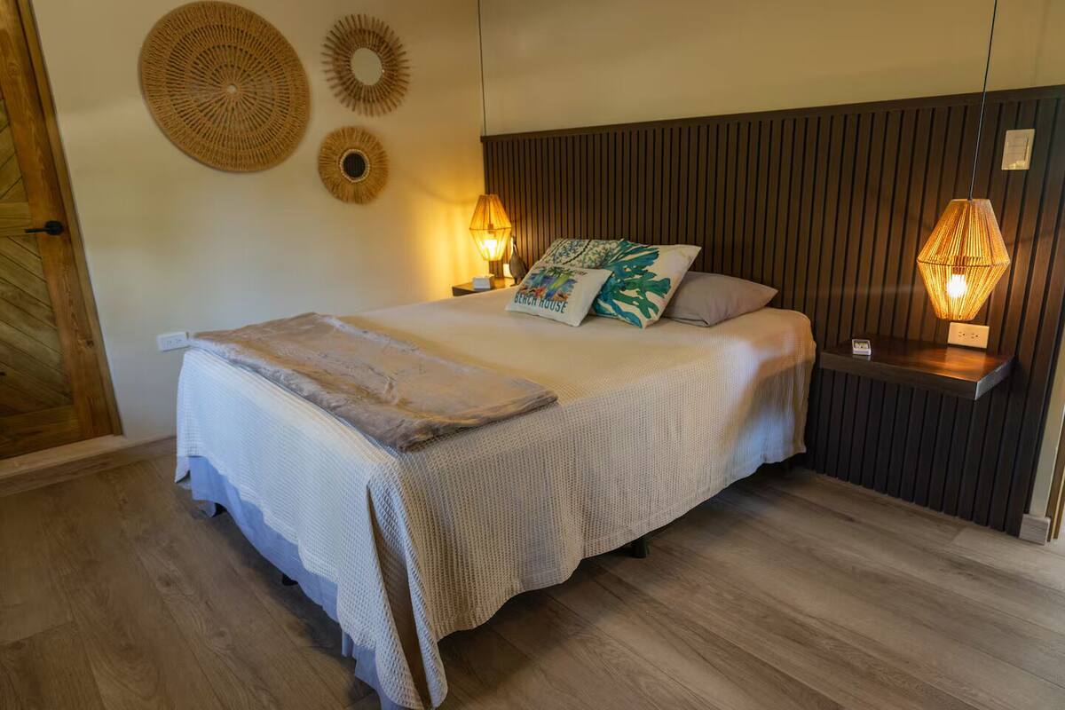 Una cama bien hecha con un edredón texturizado, dos lámparas fijadas a la pared y decoración mural.