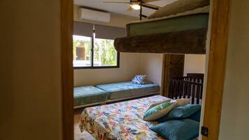 A bedroom with a bunk bed, a single bed, a ceiling fan, and a window with a view of palm trees.
