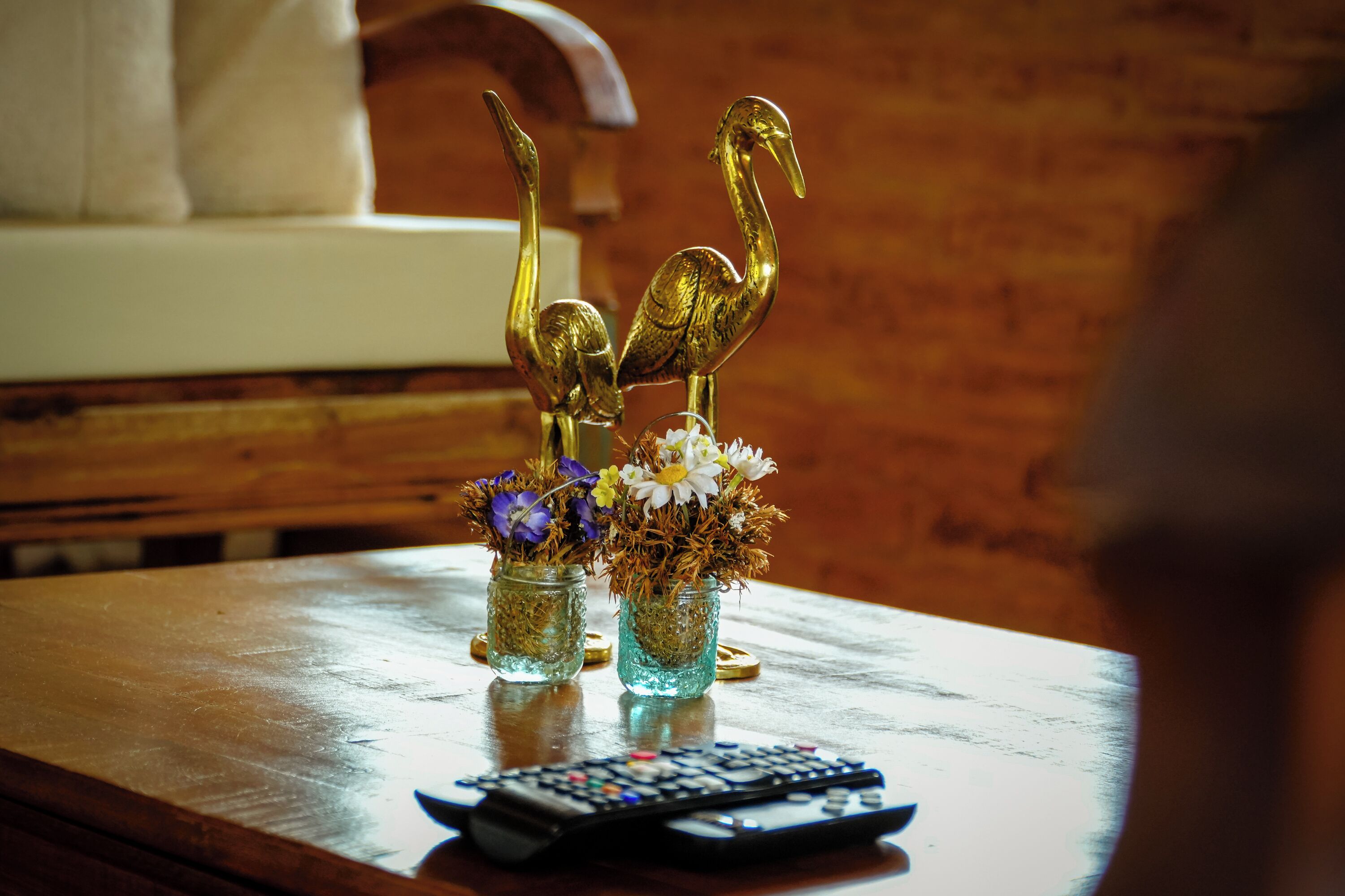 A wooden table with two glass vases containing flowers and golden swan decorations, and a remote control.