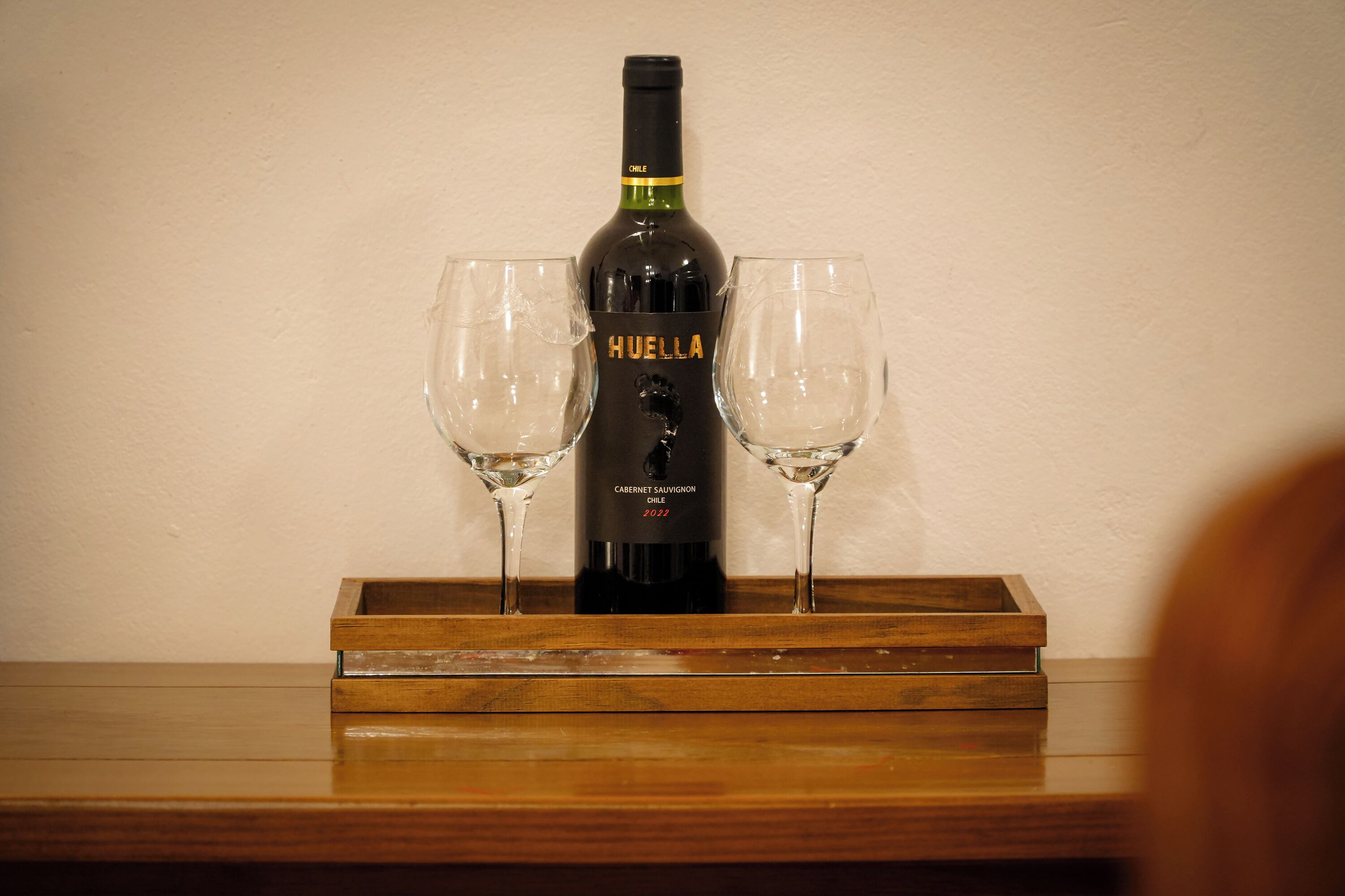 Una botella de Huelha Cabernet Sauvignon 2022 sobre una bandeja de madera con dos copas.