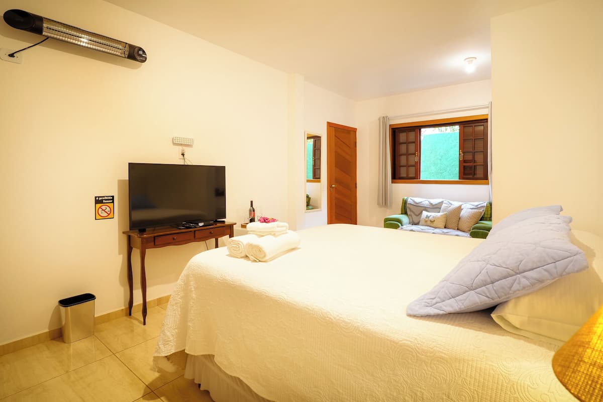 A hotel room with a bed, a television, a heater, and a window with curtains.