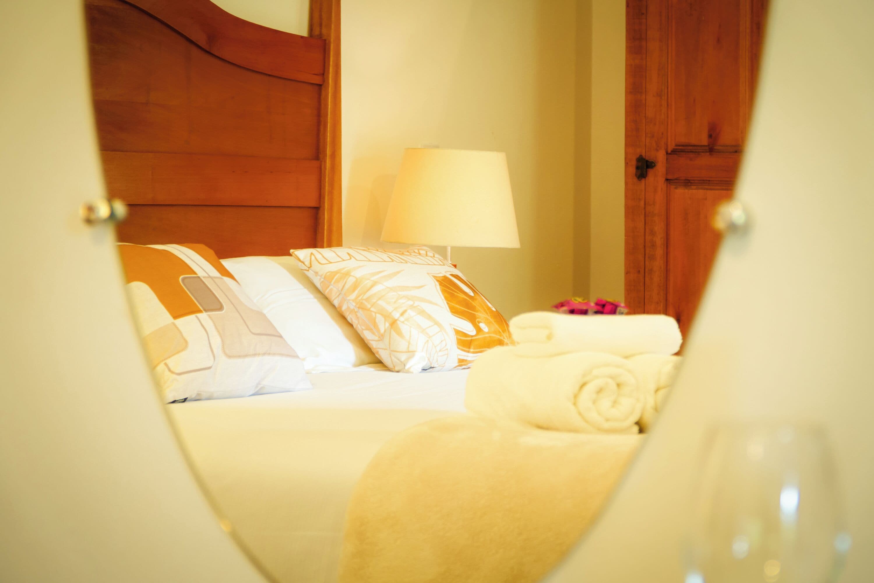 A hotel room with a bed, a nightstand, a lamp, and a wooden door.