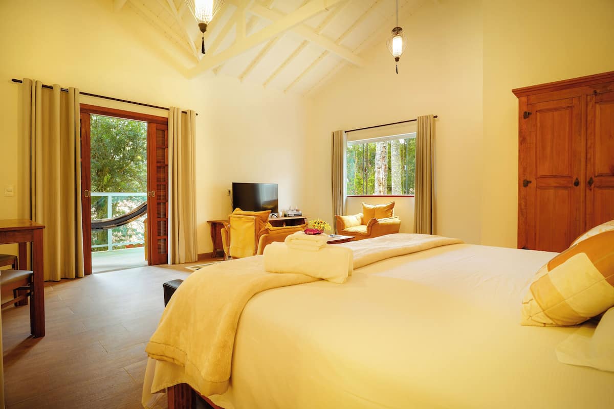 A hotel room with a large bed, a desk, a television, and a balcony with curtains.